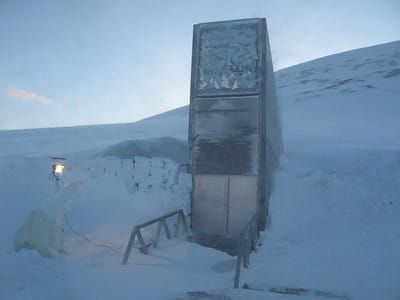 The entrance to Svalbard Global Seed Vault, buried in snow, with an ice sculpture of a polar bear next to it.